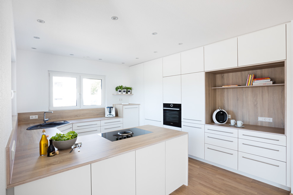 Exempel på ett stort modernt kök, med en nedsänkt diskho, släta luckor, vita skåp, laminatbänkskiva, brunt stänkskydd, stänkskydd i trä, svarta vitvaror, en halv köksö och brunt golv