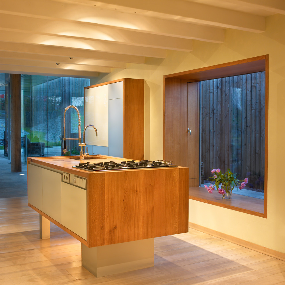 Bild på ett stort funkis brun brunt kök, med en integrerad diskho, luckor med profilerade fronter, grå skåp, träbänkskiva, gult stänkskydd, stänkskydd i stenkakel, rostfria vitvaror, ljust trägolv, flera köksöar och brunt golv