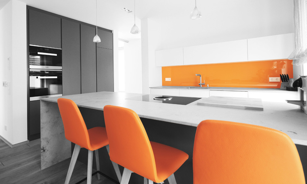 Foto på ett stort funkis kök, med en enkel diskho, släta luckor, marmorbänkskiva, orange stänkskydd, glaspanel som stänkskydd, svarta vitvaror, mellanmörkt trägolv och en köksö