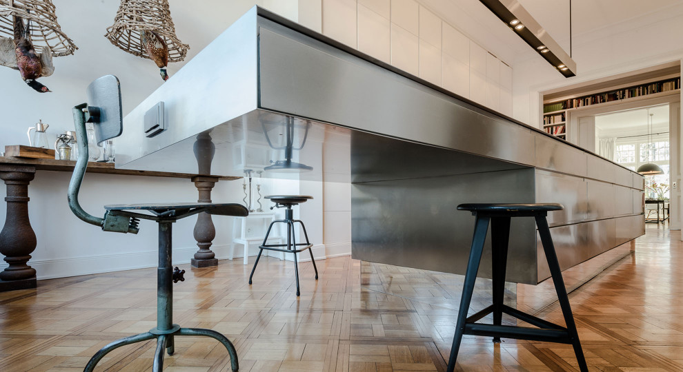 Diseño de cocina minimalista grande abierta con armarios con paneles lisos, puertas de armario blancas, encimera de acero inoxidable, suelo de madera en tonos medios y una isla