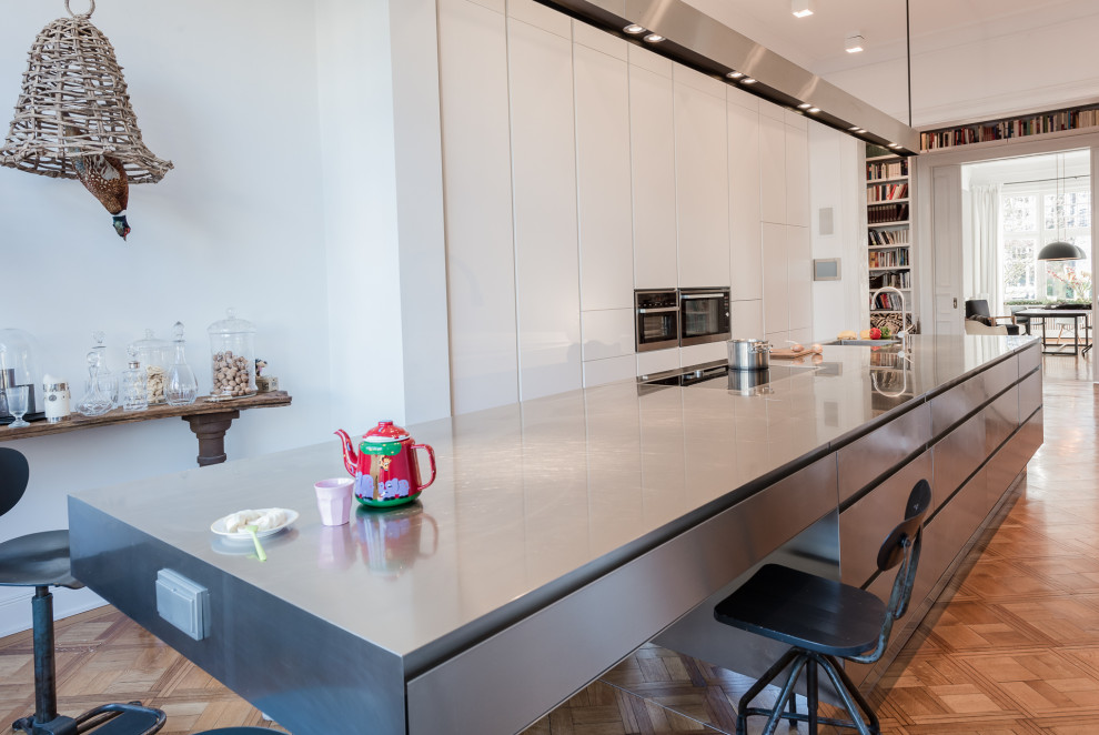 Ejemplo de cocina minimalista grande abierta con armarios con paneles lisos, encimera de acero inoxidable, suelo de madera en tonos medios y una isla