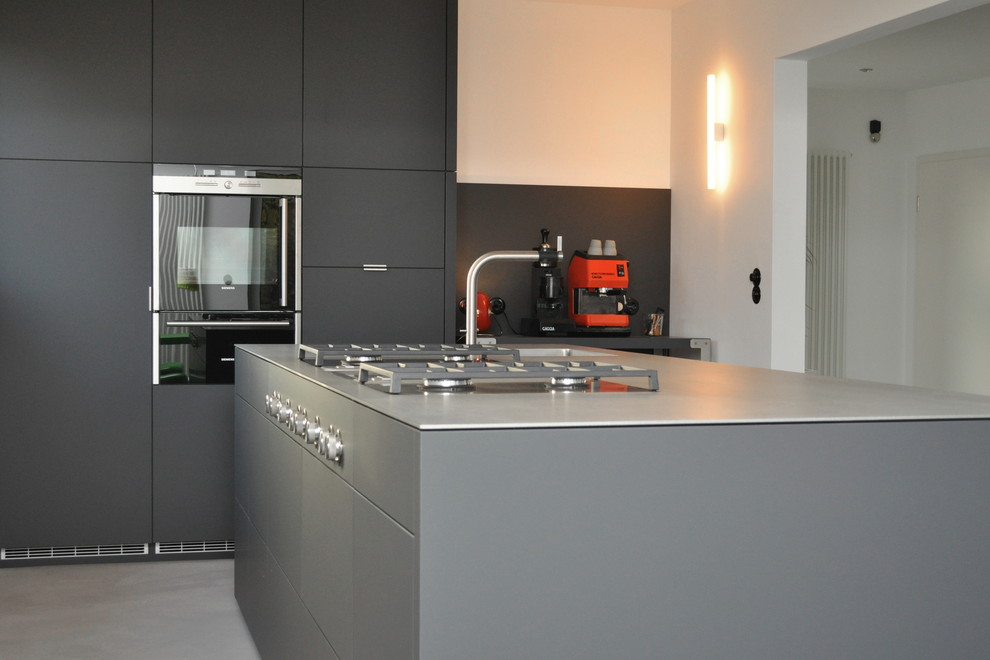 Moderne Küche mit flächenbündigen Schrankfronten, grauen Schränken, Edelstahl-Arbeitsplatte und Kücheninsel in Essen