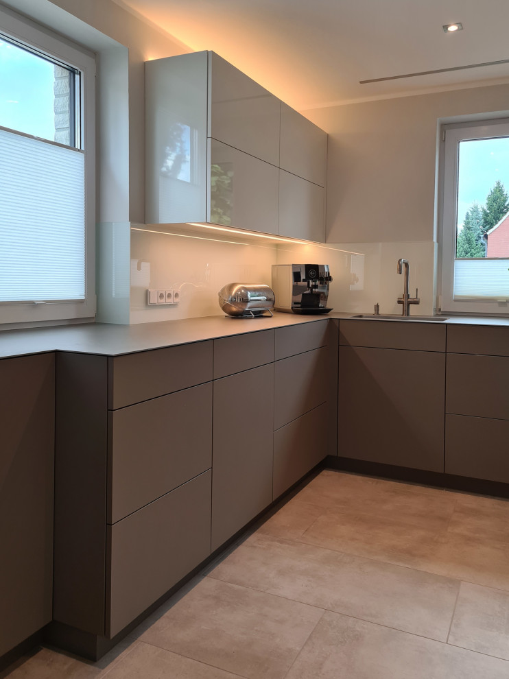 Cette image montre une cuisine design en U fermée et de taille moyenne avec un placard à porte plane, des portes de placard grises, un plan de travail en inox, une crédence en feuille de verre et un électroménager noir.