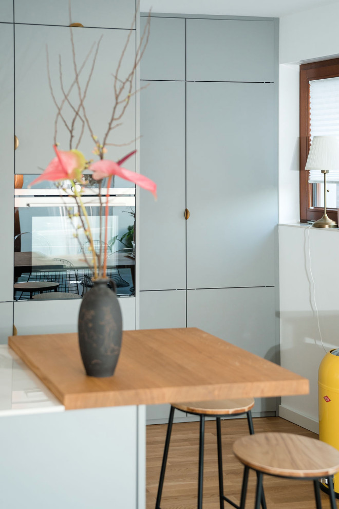 Идея дизайна: параллельная кухня среднего размера в скандинавском стиле с обеденным столом, врезной мойкой, плоскими фасадами, серыми фасадами, розовым фартуком, черной техникой, светлым паркетным полом, островом и белой столешницей