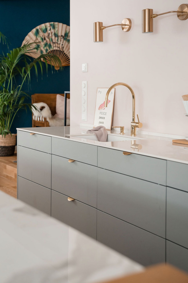 Photo of a medium sized scandinavian galley kitchen/diner in Other with a submerged sink, flat-panel cabinets, grey cabinets, pink splashback, black appliances, light hardwood flooring, an island and white worktops.