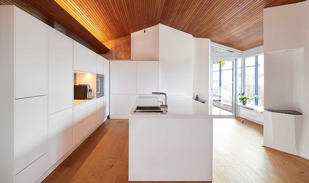 Offene, Große Moderne Küche in L-Form mit flächenbündigen Schrankfronten, weißen Schränken, braunem Holzboden, Kücheninsel und braunem Boden in Stuttgart
