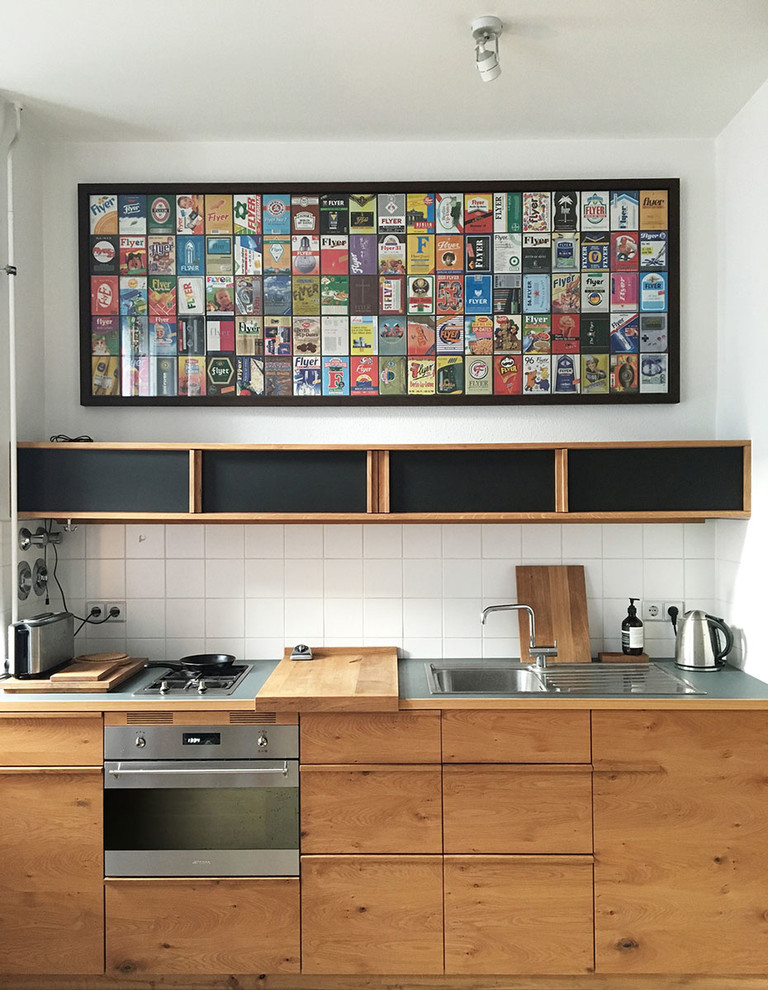 ベルリンにある小さなコンテンポラリースタイルのおしゃれなキッチン (ドロップインシンク、フラットパネル扉のキャビネット、中間色木目調キャビネット、白いキッチンパネル、セラミックタイルのキッチンパネル、シルバーの調理設備) の写真