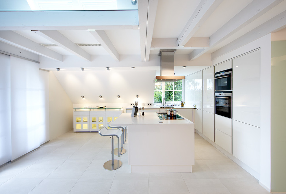 На фото: угловая, глянцевая кухня-гостиная среднего размера в современном стиле с плоскими фасадами, белыми фасадами, техникой под мебельный фасад, островом, двойной мойкой и мойкой у окна с