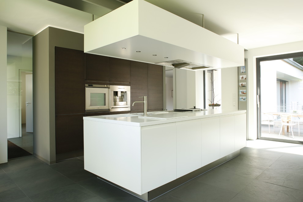 Modern inredning av ett stort kök med öppen planlösning, med en integrerad diskho, släta luckor, skåp i mörkt trä, grått stänkskydd, rostfria vitvaror, skiffergolv och en köksö