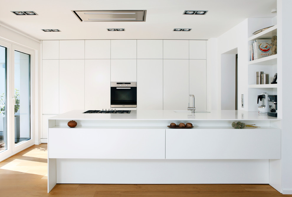 Immagine di una cucina design chiusa e di medie dimensioni con ante lisce, ante bianche, elettrodomestici in acciaio inossidabile, parquet chiaro e penisola