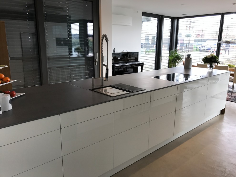Large contemporary single-wall open plan kitchen in Other with a built-in sink, flat-panel cabinets, white cabinets, concrete worktops, white splashback, stainless steel appliances, concrete flooring, an island, beige floors and grey worktops.
