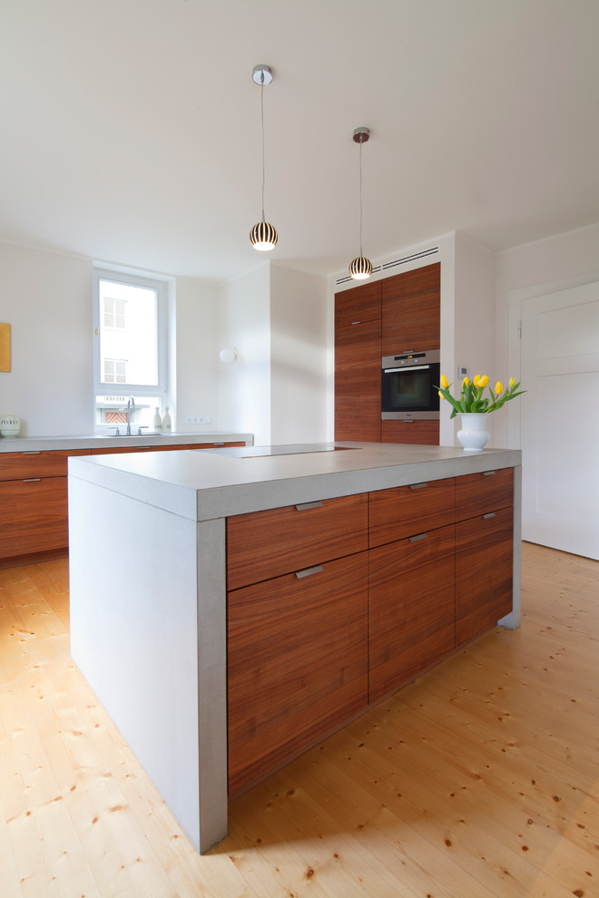Idée de décoration pour une cuisine encastrable design en bois brun fermée et de taille moyenne avec un placard à porte plane, parquet clair et îlot.