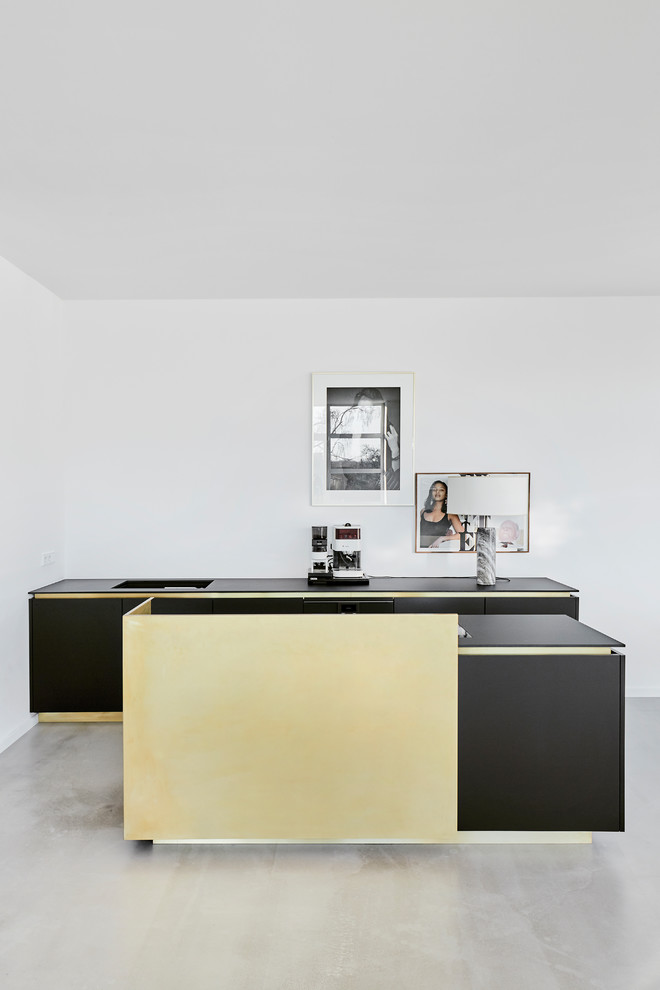 Modelo de cocina moderna pequeña abierta con armarios con paneles lisos, salpicadero blanco, suelo de cemento, una isla, suelo gris y encimeras negras