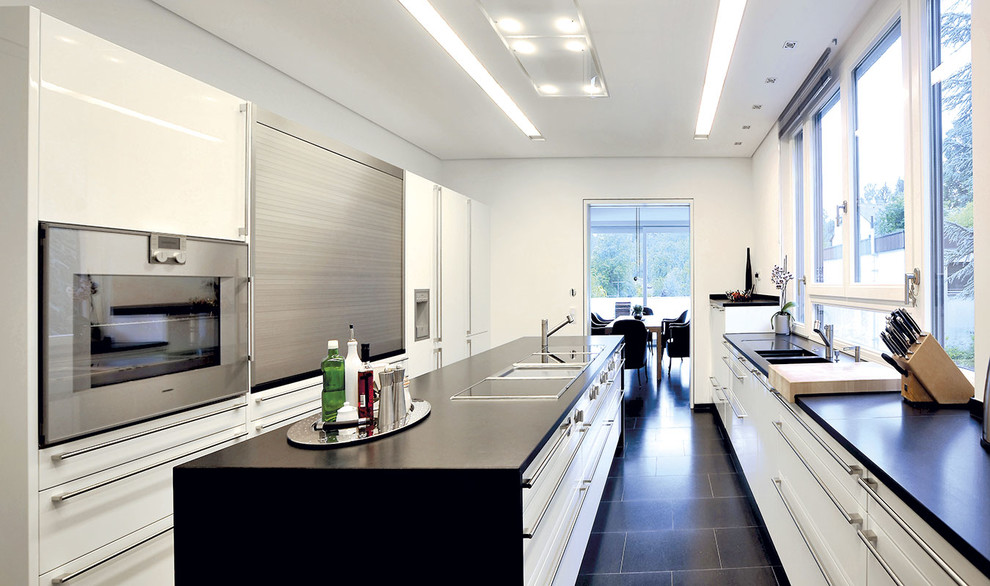 Inspiration pour une grande cuisine parallèle design avec un placard à porte plane, des portes de placard blanches, un électroménager en acier inoxydable, un sol en carrelage de céramique, îlot et un sol noir.