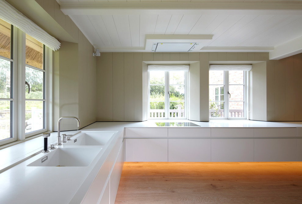 Moderne Küche in L-Form mit flächenbündigen Schrankfronten, weißen Schränken, hellem Holzboden, Doppelwaschbecken und Elektrogeräten mit Frontblende in München