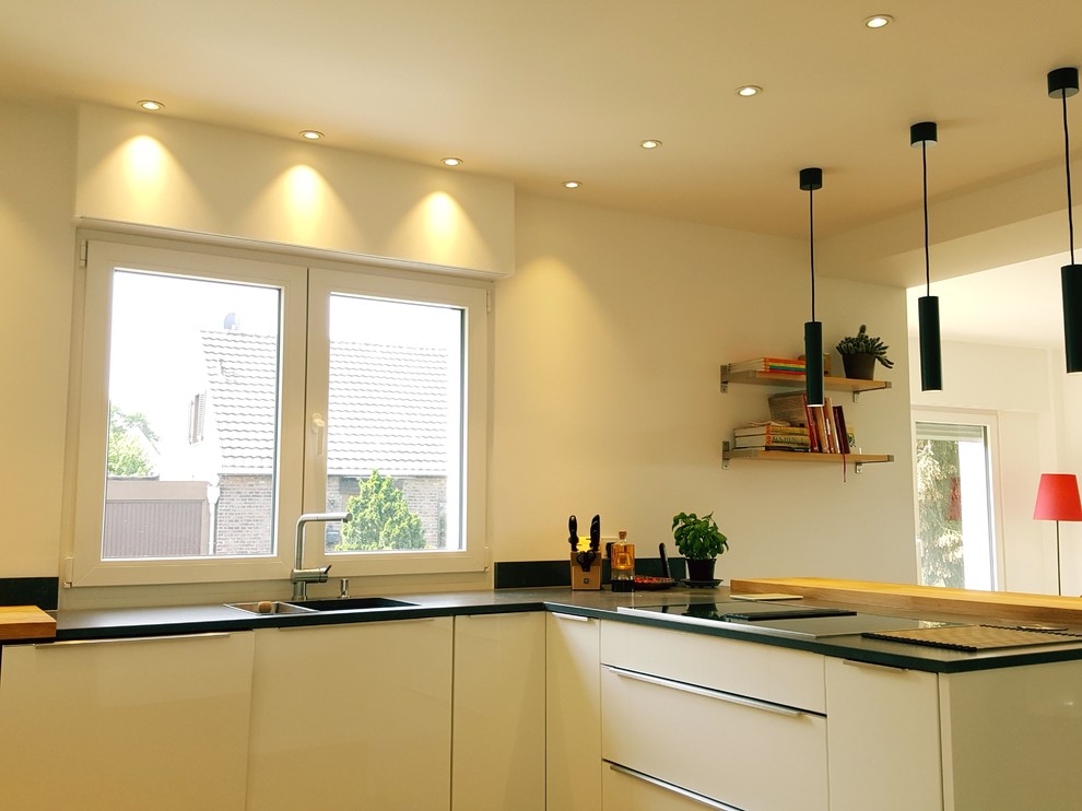 На фото: п-образная кухня-гостиная среднего размера в стиле модернизм с плоскими фасадами, белыми фасадами, гранитной столешницей, белым фартуком, полуостровом и черной столешницей