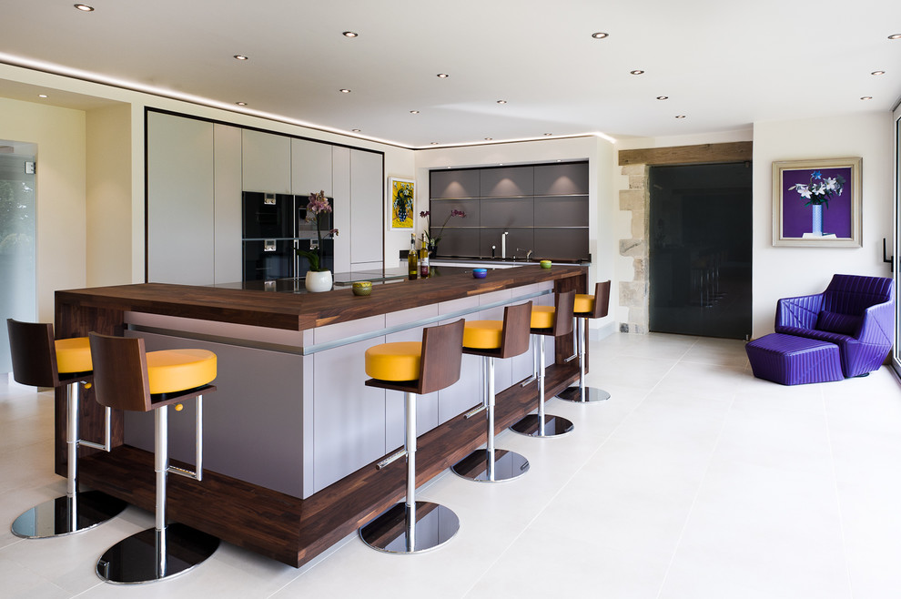 Moderne Küche in U-Form mit flächenbündigen Schrankfronten, grauen Schränken, Arbeitsplatte aus Holz, schwarzen Elektrogeräten, Kücheninsel, weißem Boden und brauner Arbeitsplatte in Stuttgart