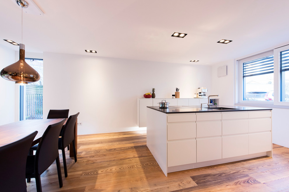 Modern inredning av ett mellanstort kök, med en undermonterad diskho, släta luckor, vita skåp, vitt stänkskydd, rostfria vitvaror, målat trägolv och en köksö