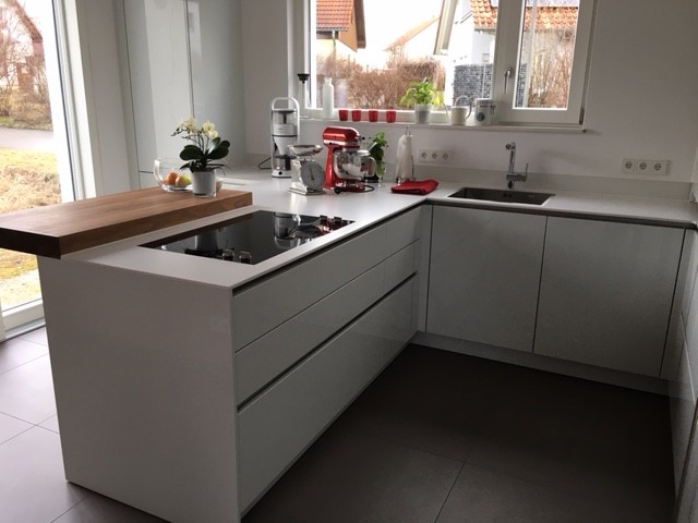 Modern inredning av ett stort kök, med en nedsänkt diskho, släta luckor, vita skåp, rostfria vitvaror, en halv köksö, grått golv och betonggolv