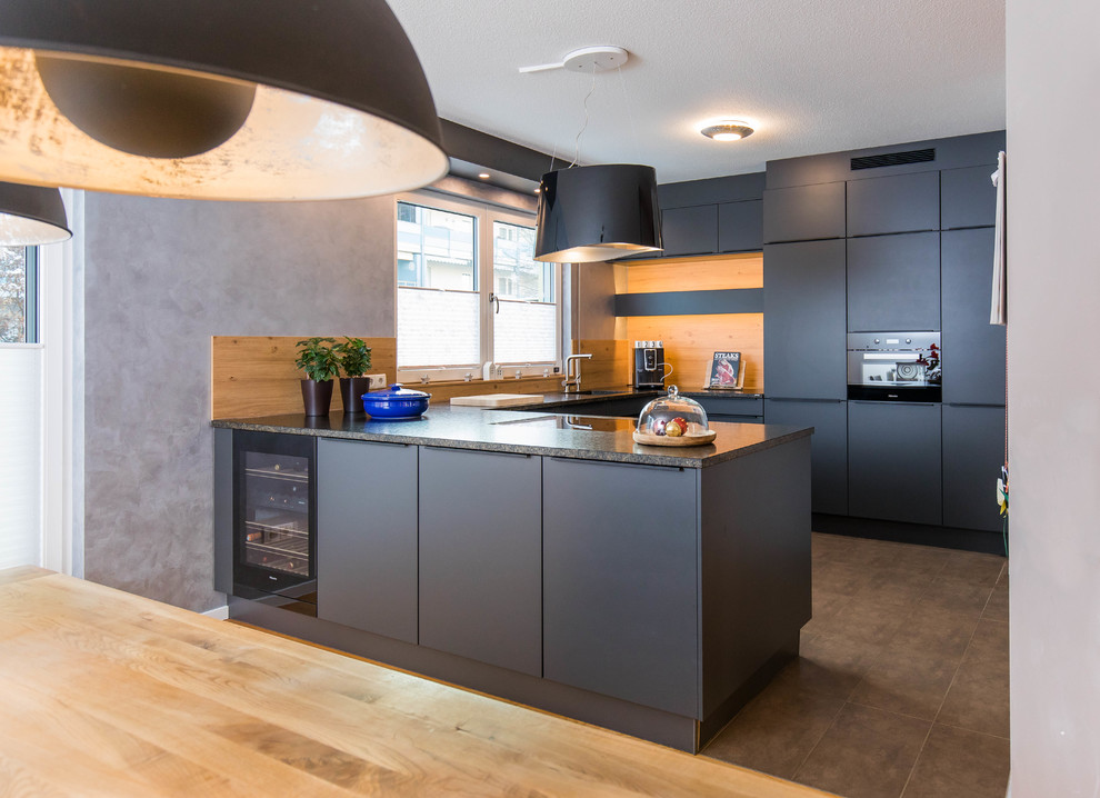 Foto på ett mellanstort funkis kök, med svarta skåp, granitbänkskiva, en halv köksö, en integrerad diskho, släta luckor, brunt stänkskydd, stänkskydd i trä, svarta vitvaror och brunt golv