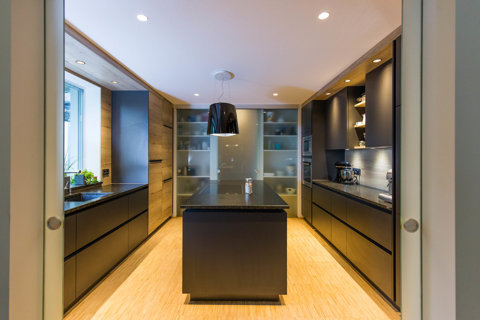 Foto på ett avskilt, mellanstort funkis svart u-kök, med en integrerad diskho, släta luckor, svarta skåp, beige stänkskydd, stänkskydd i trä, rostfria vitvaror, bambugolv, en köksö och beiget golv