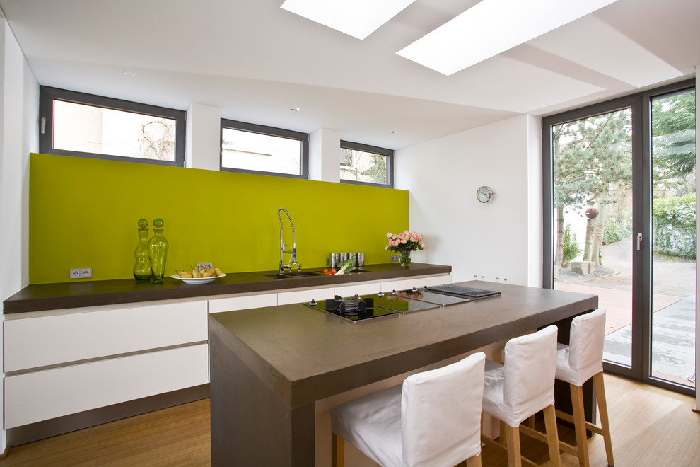 На фото: отдельная, прямая кухня среднего размера в современном стиле с тройной мойкой, плоскими фасадами, белыми фасадами, зеленым фартуком, светлым паркетным полом и островом с