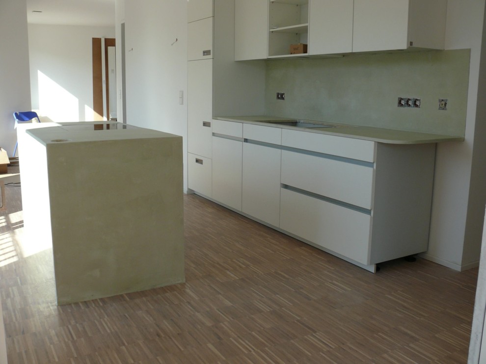 This is an example of an expansive traditional single-wall kitchen/diner in Leipzig with flat-panel cabinets, white cabinets, concrete worktops, beige splashback, dark hardwood flooring, an island and brown floors.