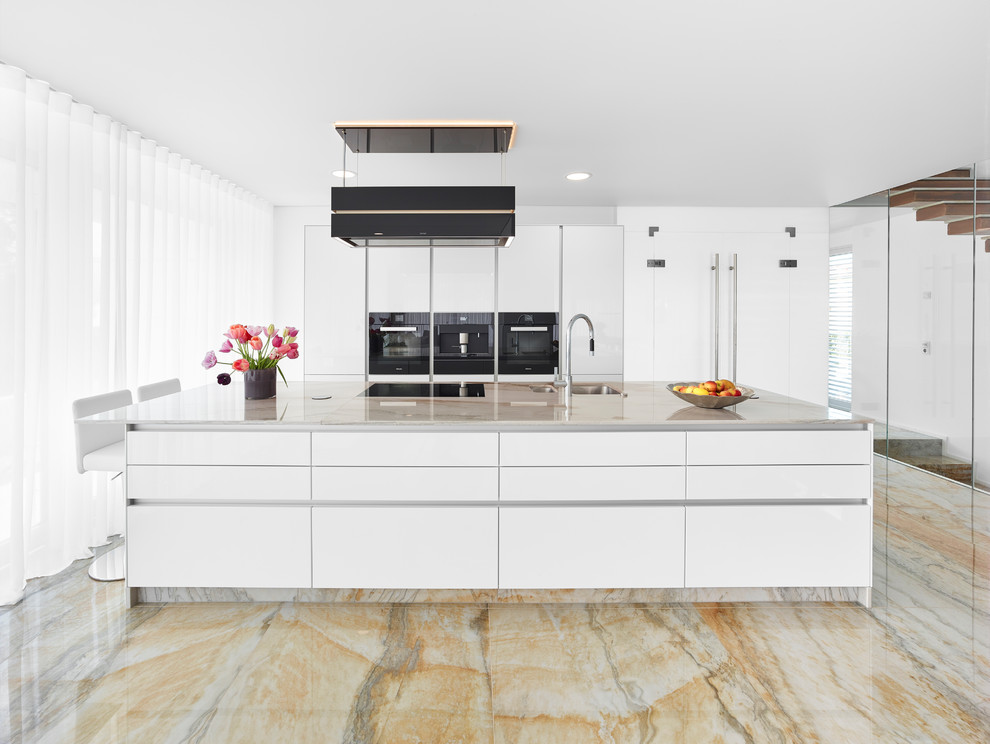 Exempel på ett mellanstort modernt linjärt kök med öppen planlösning, med vita skåp, bänkskiva i kvartsit, svarta vitvaror, en köksö, en nedsänkt diskho, släta luckor, marmorgolv och flerfärgat golv