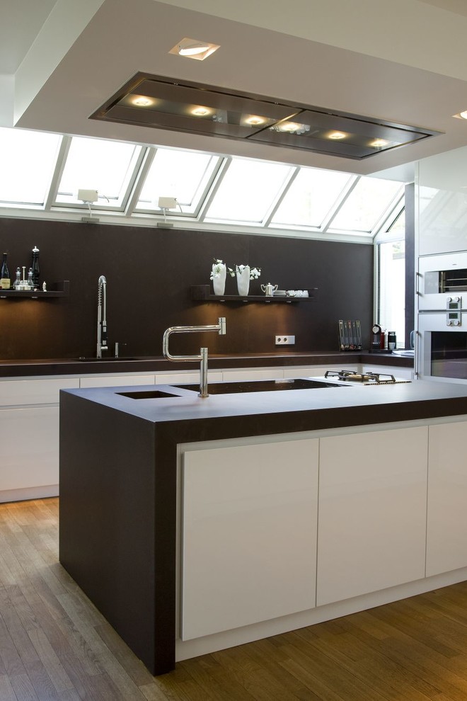 Immagine di una cucina design con lavello sottopiano, ante lisce, ante bianche, paraspruzzi marrone, pavimento in legno massello medio e elettrodomestici in acciaio inossidabile