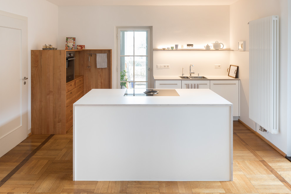 Inspiration for a large contemporary l-shaped open plan kitchen in Stuttgart with flat-panel cabinets, laminate countertops, white splashback, stainless steel appliances, white worktops, a submerged sink, white cabinets, medium hardwood flooring, an island and brown floors.