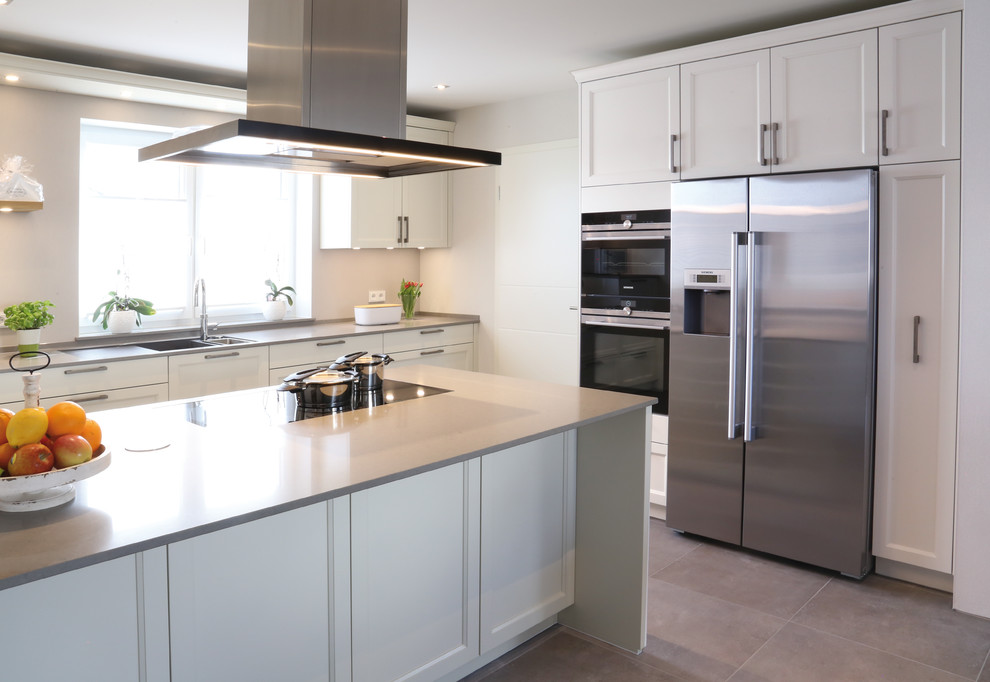 Idéer för att renovera ett mellanstort funkis grå grått kök, med en integrerad diskho, vita skåp, svarta vitvaror, en halv köksö, grått golv, luckor med profilerade fronter, granitbänkskiva, beige stänkskydd, fönster som stänkskydd och klinkergolv i porslin