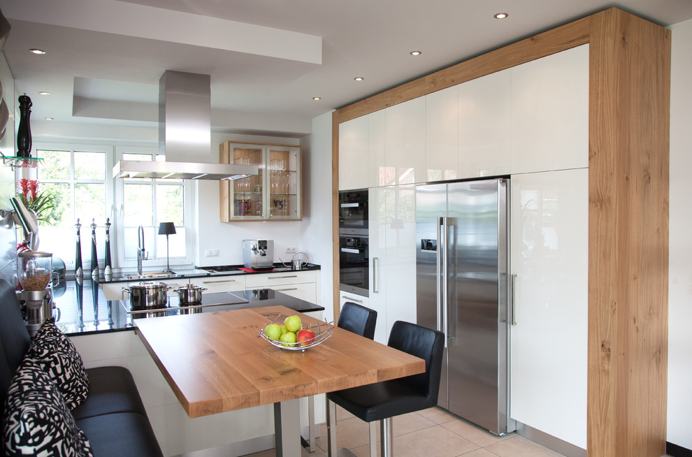 Diseño de cocinas en U actual, de tamaño medio, abierto, con fregadero integrado, armarios con paneles lisos, puertas de armario blancas, encimera de granito, salpicadero blanco, salpicadero de vidrio, electrodomésticos de acero inoxidable, una isla y suelo beige