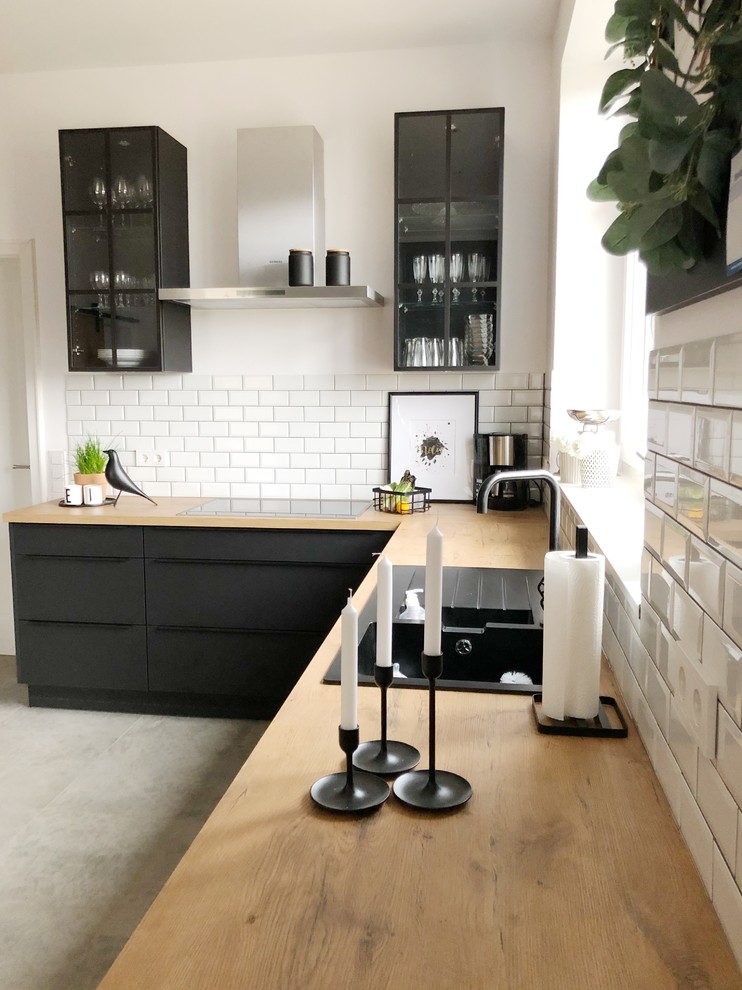 Photo of a medium sized urban open plan kitchen in Bremen with a built-in sink, flat-panel cabinets, black cabinets, white splashback, ceramic splashback, black appliances, slate flooring, grey floors and brown worktops.