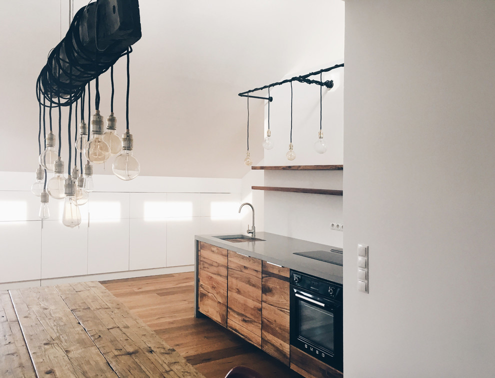 Foto di una cucina industriale di medie dimensioni con lavello integrato, ante lisce, ante in legno scuro, top in cemento, paraspruzzi bianco, elettrodomestici neri e pavimento in legno massello medio