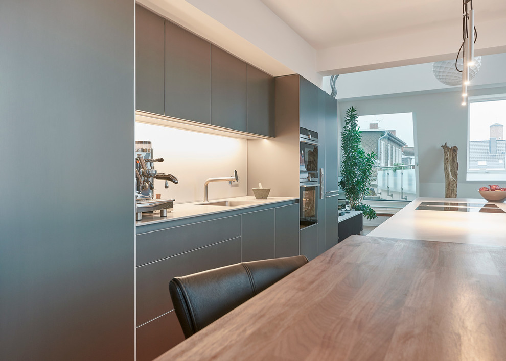 Offene, Einzeilige Moderne Küche mit grauen Schränken, schwarzen Elektrogeräten und Kücheninsel in Hannover
