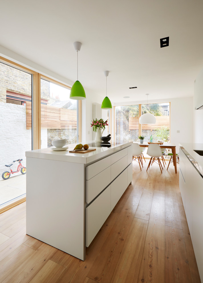 Inspiration for a medium sized contemporary single-wall open plan kitchen in London with a built-in sink, white cabinets, white splashback, medium hardwood flooring, an island, brown floors and flat-panel cabinets.