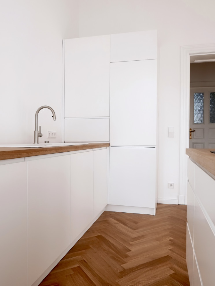 Moderne Küche mit Einbauwaschbecken, flächenbündigen Schrankfronten, weißen Schränken, Arbeitsplatte aus Holz, gebeiztem Holzboden, Kücheninsel, braunem Boden und brauner Arbeitsplatte in Berlin