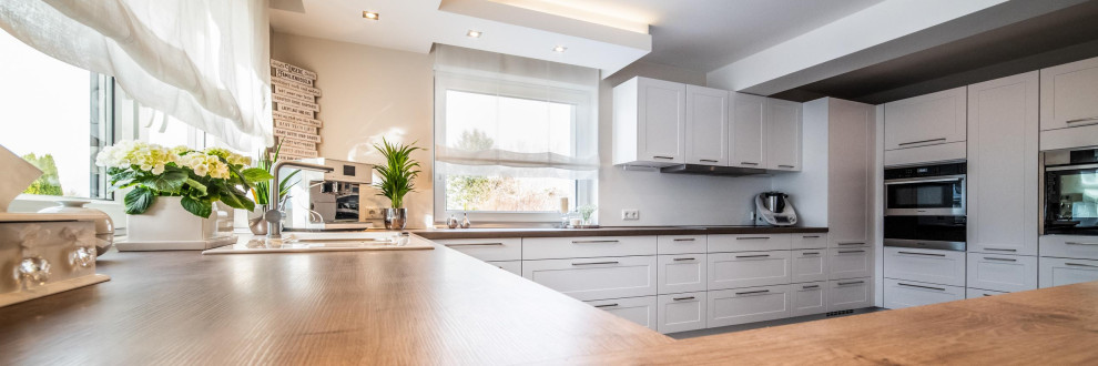 Inspiration for a large contemporary u-shaped open plan kitchen in Hanover with an integrated sink, raised-panel cabinets, white cabinets, wood worktops, white splashback, wood splashback, stainless steel appliances, vinyl flooring, a breakfast bar, brown floors and brown worktops.
