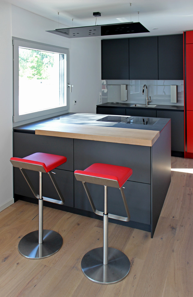 Exempel på ett modernt svart svart parallellkök, med en enkel diskho, släta luckor, svarta skåp, grått stänkskydd, glaspanel som stänkskydd, ljust trägolv, en halv köksö och beiget golv