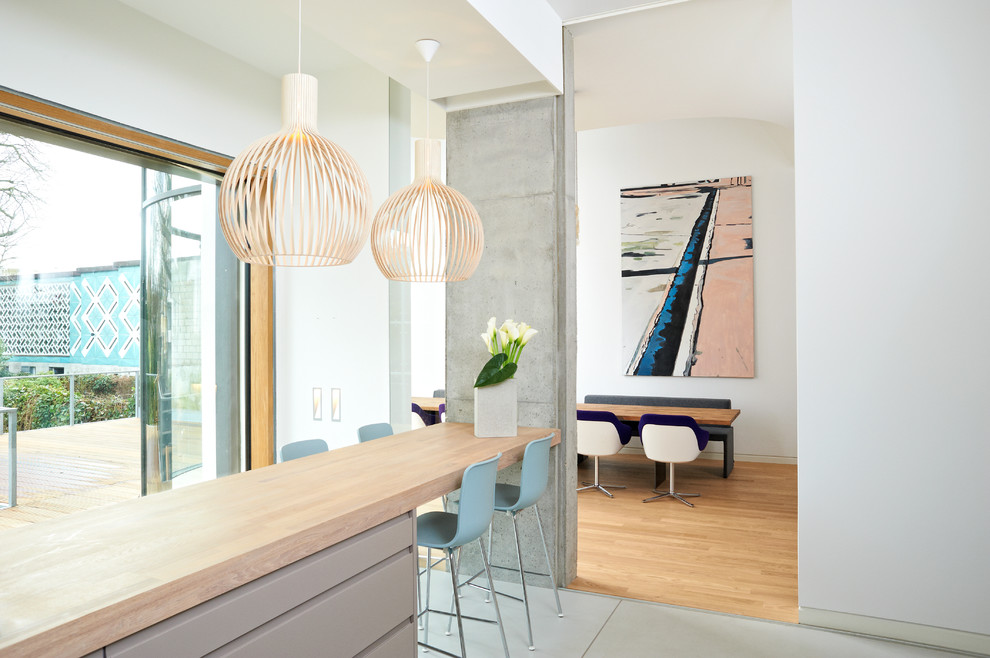 На фото: кухня-гостиная в современном стиле с плоскими фасадами, серыми фасадами, деревянной столешницей, бетонным полом, полуостровом и окном с