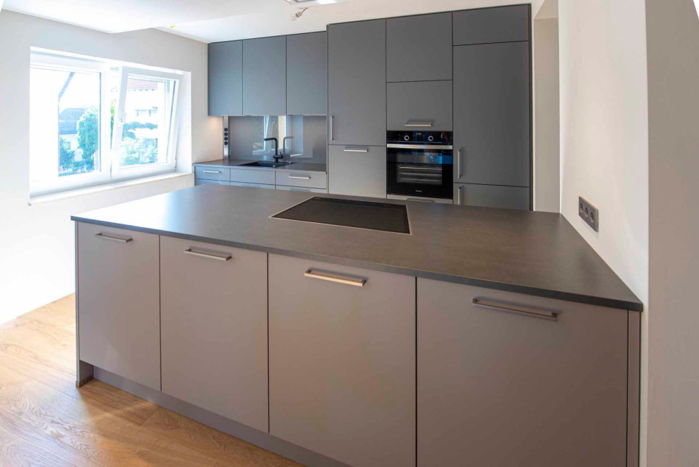 Photo of a medium sized contemporary single-wall open plan kitchen in Frankfurt with a built-in sink, flat-panel cabinets, grey cabinets, wood worktops, grey splashback, wood splashback, integrated appliances, a breakfast bar, grey worktops and a drop ceiling.