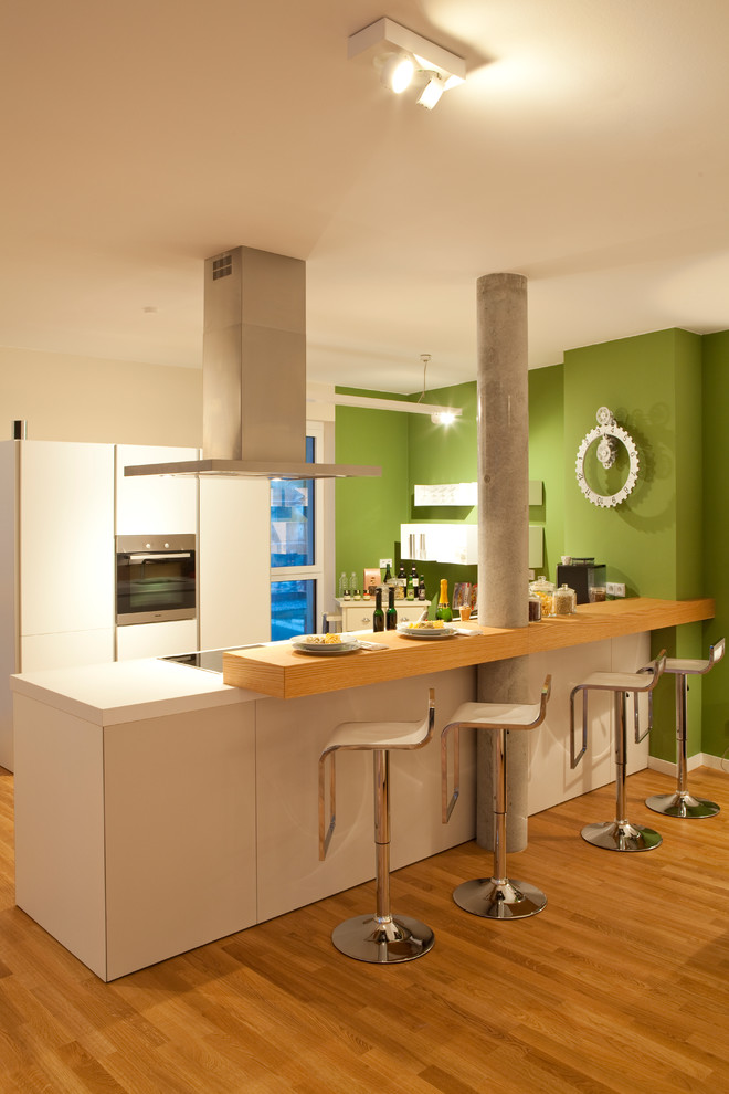 Modelo de cocinas en L contemporánea de tamaño medio abierta con armarios con paneles lisos, puertas de armario blancas, suelo de madera en tonos medios, península y electrodomésticos con paneles