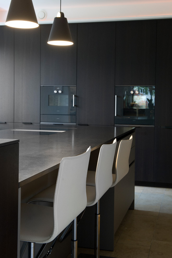 Moderne Küche mit flächenbündigen Schrankfronten, schwarzen Schränken, Granit-Arbeitsplatte, schwarzen Elektrogeräten, Porzellan-Bodenfliesen und beigem Boden in Sonstige