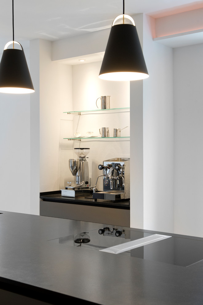 Moderne Küche mit flächenbündigen Schrankfronten, schwarzen Schränken, Granit-Arbeitsplatte, schwarzen Elektrogeräten, Porzellan-Bodenfliesen und beigem Boden in Sonstige