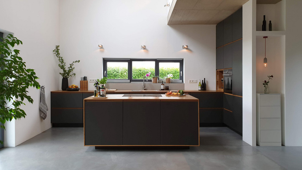 Свежая идея для дизайна: кухня-гостиная в скандинавском стиле с накладной мойкой, плоскими фасадами, черными фасадами, деревянной столешницей, бетонным полом, островом и серым полом - отличное фото интерьера