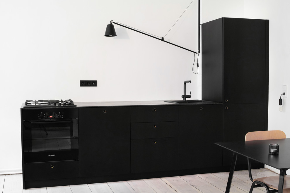 Offene, Einzeilige, Kleine Moderne Küche mit flächenbündigen Schrankfronten, schwarzen Schränken, Mineralwerkstoff-Arbeitsplatte, schwarzen Elektrogeräten und hellem Holzboden in Berlin
