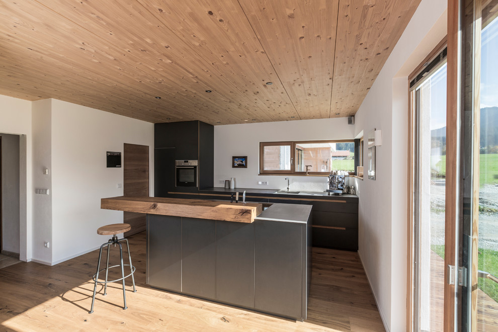 Modern inredning av ett mellanstort kök, med en integrerad diskho, släta luckor, svarta skåp, bänkskiva i rostfritt stål, ljust trägolv och en köksö
