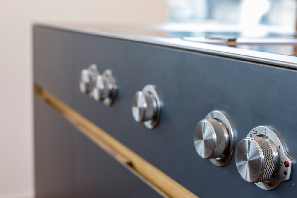 Esempio di una cucina design di medie dimensioni con lavello integrato, ante lisce, ante nere, top in acciaio inossidabile e parquet chiaro