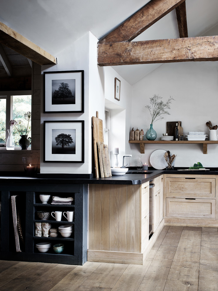 This is an example of a large farmhouse l-shaped open plan kitchen in Dusseldorf with a belfast sink, shaker cabinets, light wood cabinets, white splashback, black appliances, no island and light hardwood flooring.