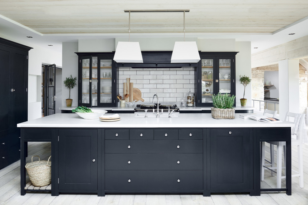 Large elegant galley painted wood floor open concept kitchen photo in Dusseldorf with glass-front cabinets, black cabinets, white backsplash, subway tile backsplash and an island